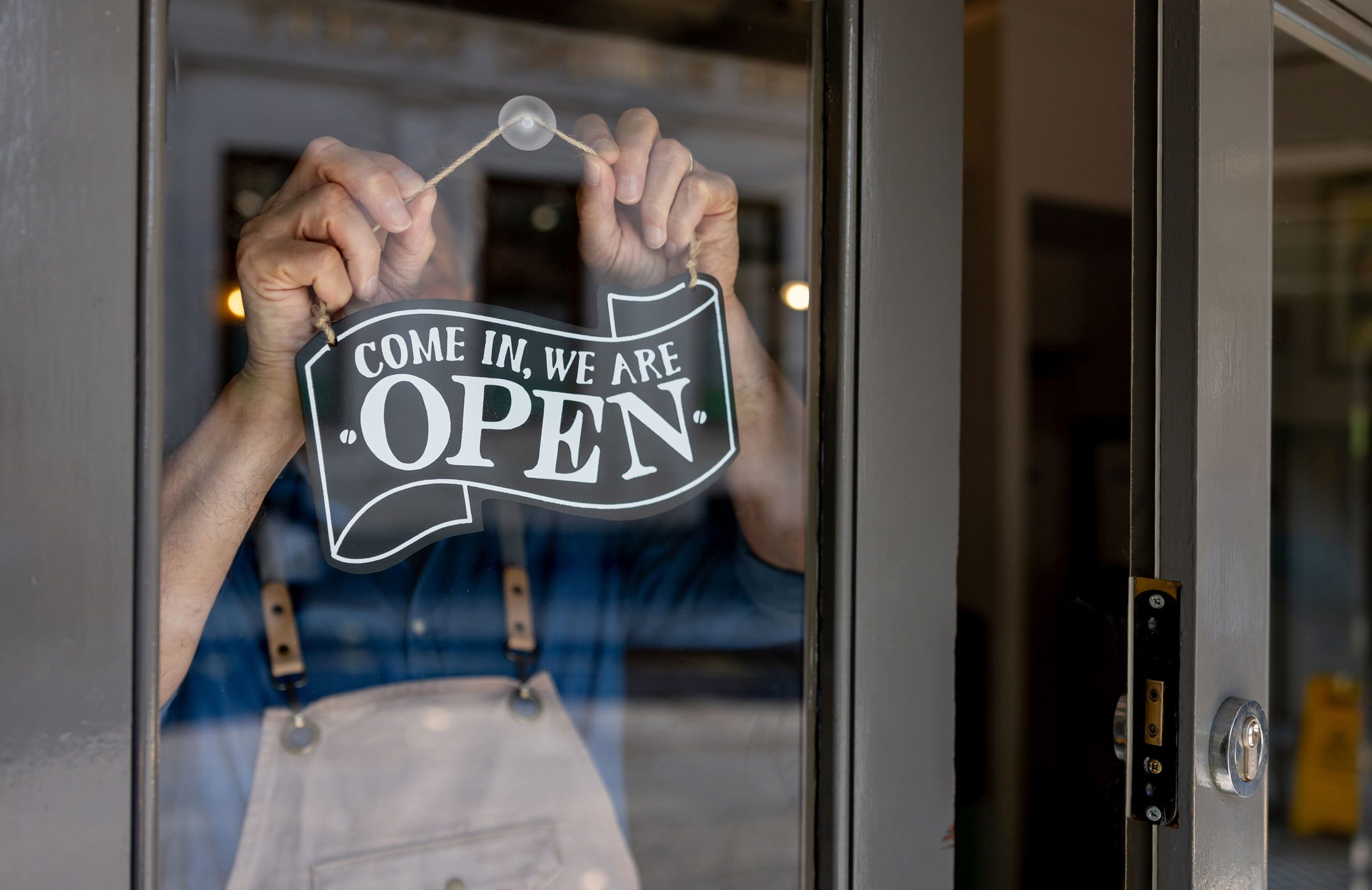 A person in overalls hangs a sign on a glass door that reads